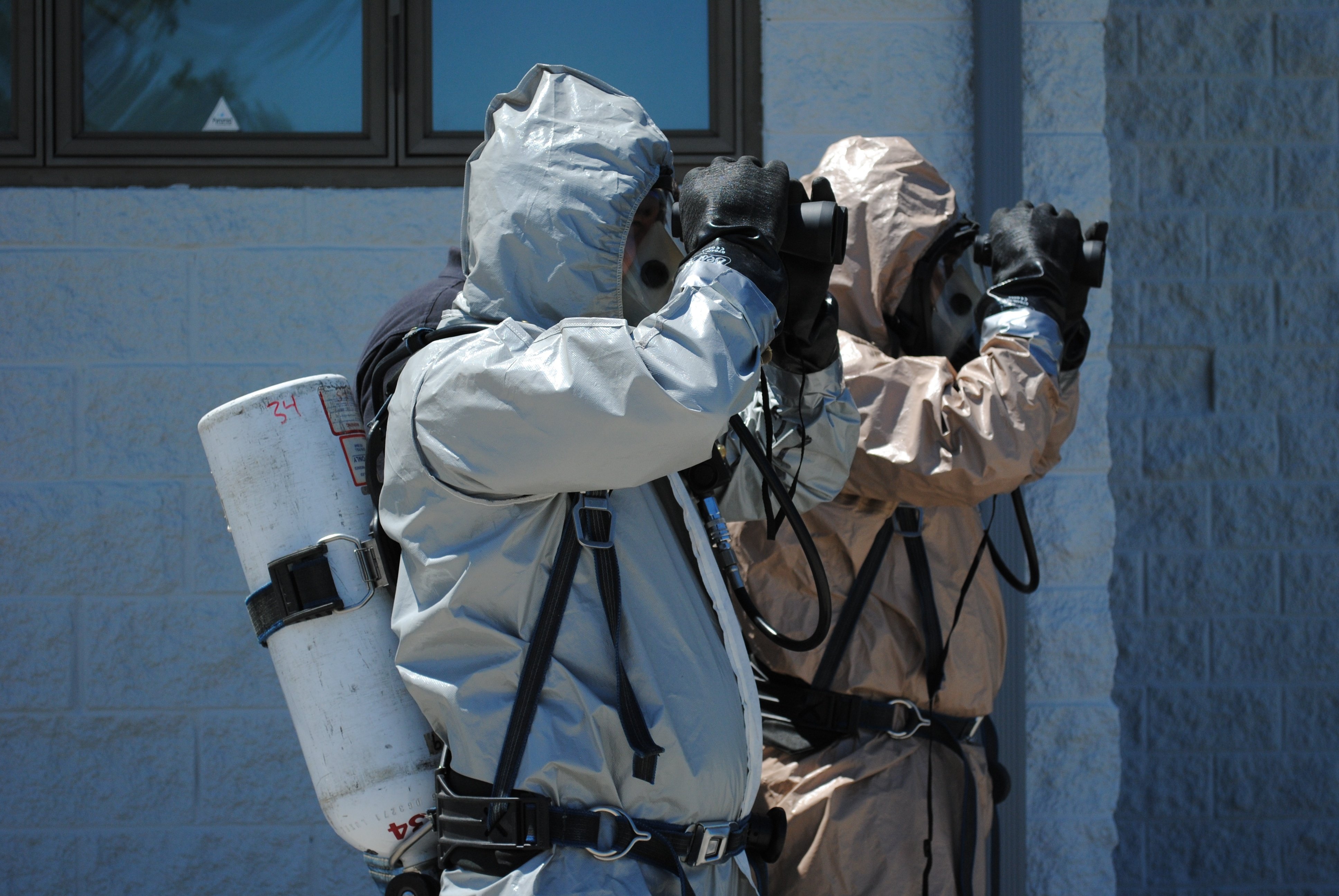 OSHA students in hazmat suits using binoculars during a training